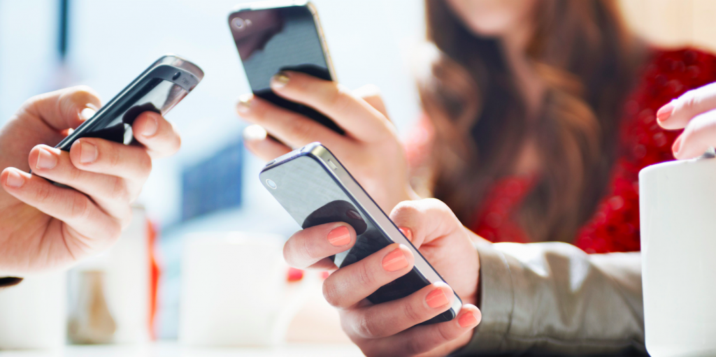 A close-up view of several people's hands, each holding and interacting with their own smartphone, highlighting themes of digital connection and modern communication.