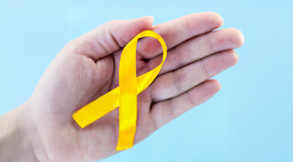 A hand holding a bright yellow suicide prevention and awareness ribbon against a light blue background.