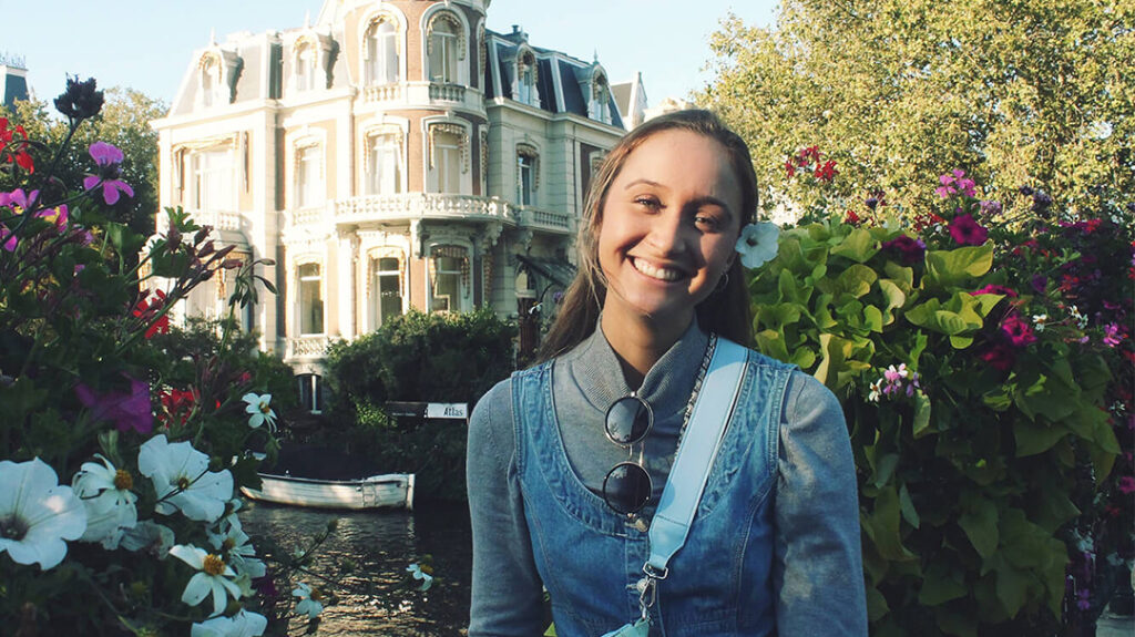 Constantina Venetis smiling outdoors in front of a historic building and lush greenery.