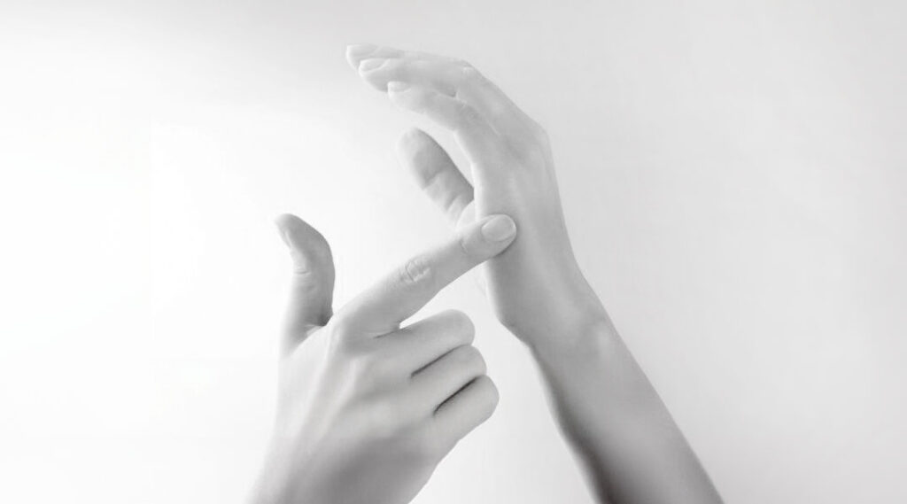A black-and-white close-up of a person's hands demonstrating the side-of-hand tapping point for emotional feeling technique (EFT).