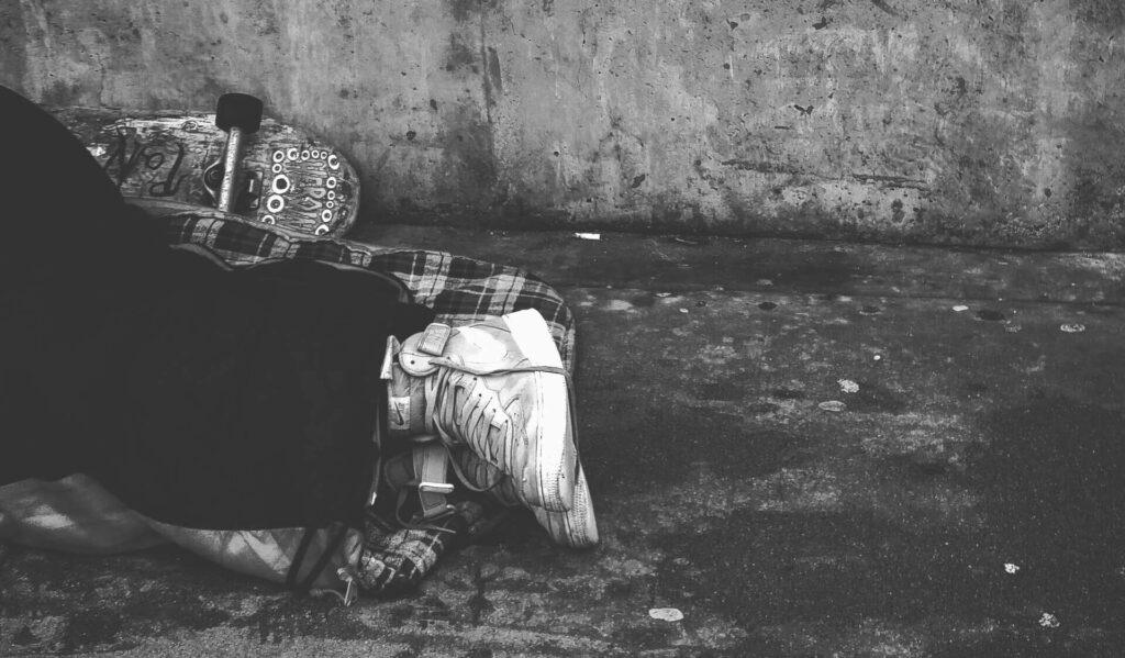 A person lying on their side on a concrete surface with a skateboard resting beside them, captured in a black and white photograph.