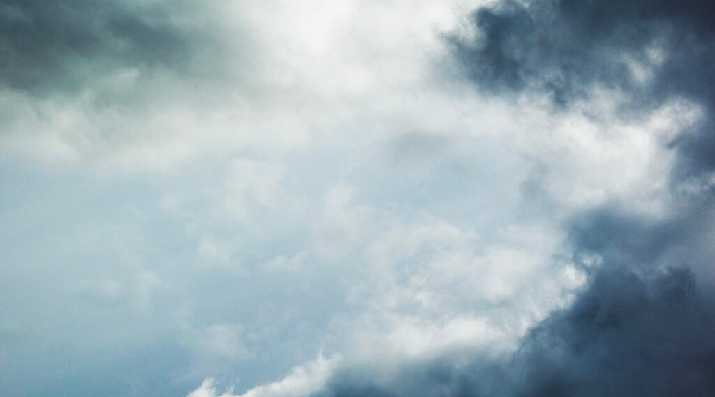 A dramatic sky filled with thick, swirling grey and dark storm clouds with a break of lighter light shining through.
