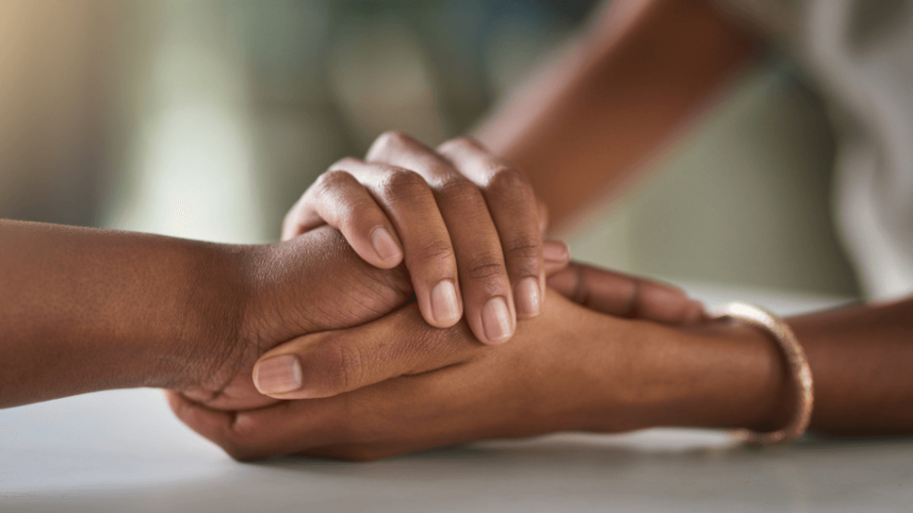 Two hands holding another person's hand in a supportive gesture.