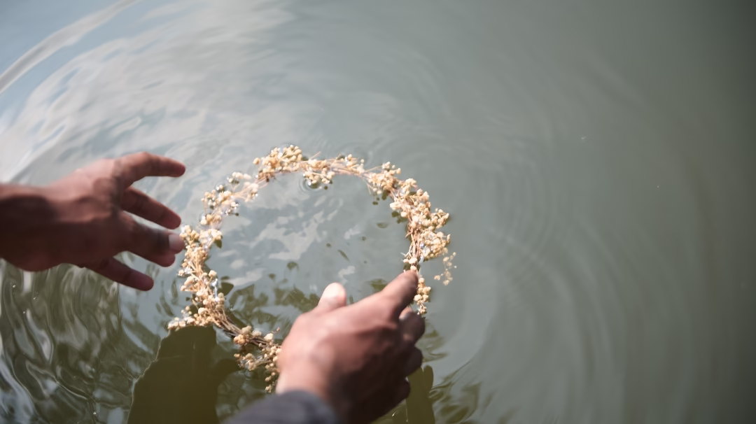 Hands letting go of a flower crown in water. Eli's Place blog about Mental Illness Grief