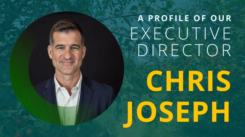 A man in a suit, Chris Joseph, who is the new Executive Director at Eli's Place. The image features a circular portrait of him against a green and dark background, with the text "A Profile of Our Executive Director Chris Joseph" overlaid in white and yellow.